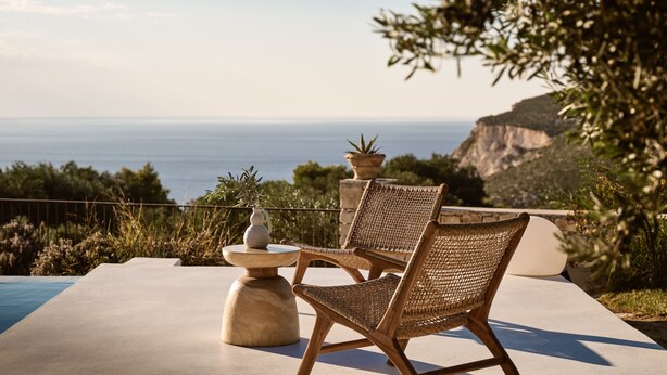 Een terras met twee rieten stoelen en een tafel, met uitzicht op een klif en de zee.