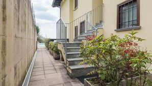 Ein schmaler Pfad führt zu einem Gebäude mit einer Treppe und einem Pool im Hintergrund.