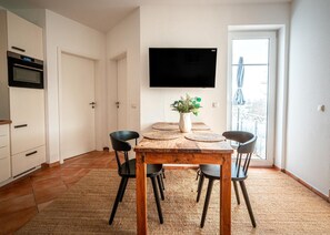 Une cuisine moderne avec des armoires blanches, un four encastré et un téléviseur à écran plat fixé au-dessus de la table à manger.