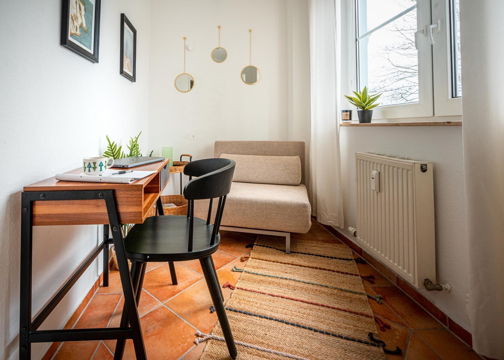 A small, cozy room with a sofa, a chair, a table with a laptop, and a radiator.