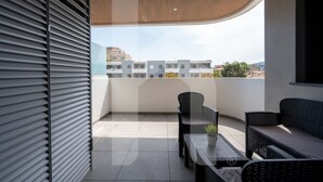 A balcony with a wooden ceiling, a black wicker sofa, a small table with a plant, and a view of buildings in the distance. - Homiday - Waterfront, Interior 9 (Borgo Santa Maria Immacolata)