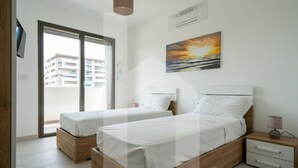 A bedroom with two beds, a TV, a painting, and a view of a building through a glass door. - Homiday - Waterfront, Interior 9 (Borgo Santa Maria Immacolata)