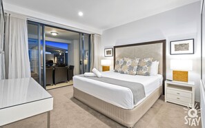 A hotel room with a large bed, a desk, a chair, a lamp, and a view of the outdoor area.