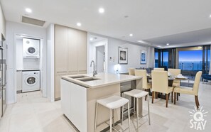 A modern kitchen with a central island, bar stools, and a dining area with a view of the sea.
