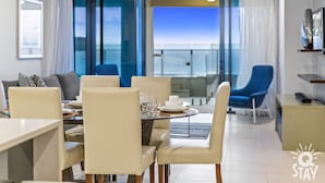 A modern dining area with a view of the sea, featuring a round table with chairs, a sofa, and a blue armchair. - 2 Bedroom Apartment With Private Plunge Pool (Surfers Paradise)