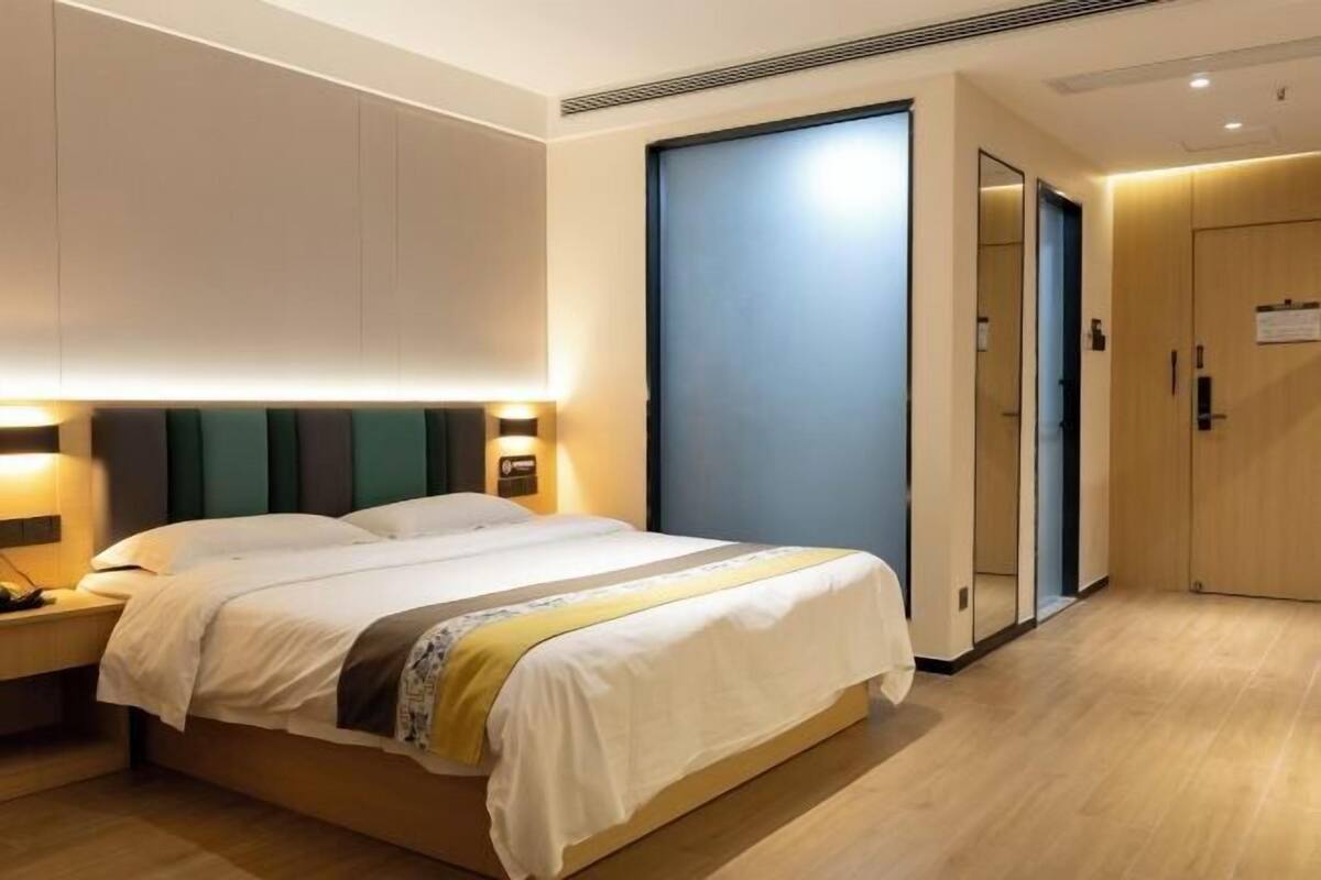 Una habitación de hotel con cama, lámparas de noche, armario y puerta.