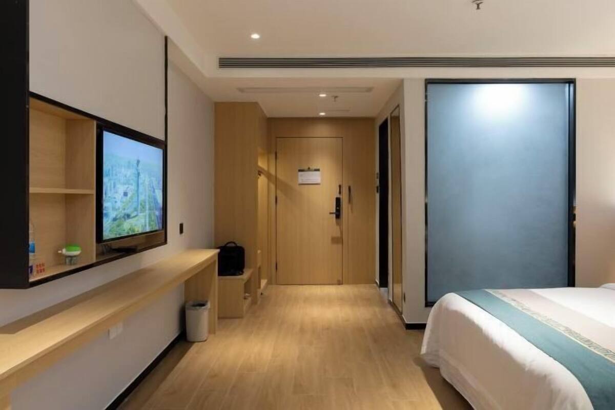 Una habitación de hotel con una cama, un televisor en la pared, suelo de madera y una puerta.