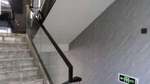 Een moderne trap met glazen leuningen en een marmeren vloer, die leidt naar een ruimte met een grijze marmeren wand en een vluchtwijzer.