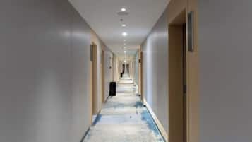 A hotel corridor with doors on both sides, a carpeted floor, and a trash bin in the center.