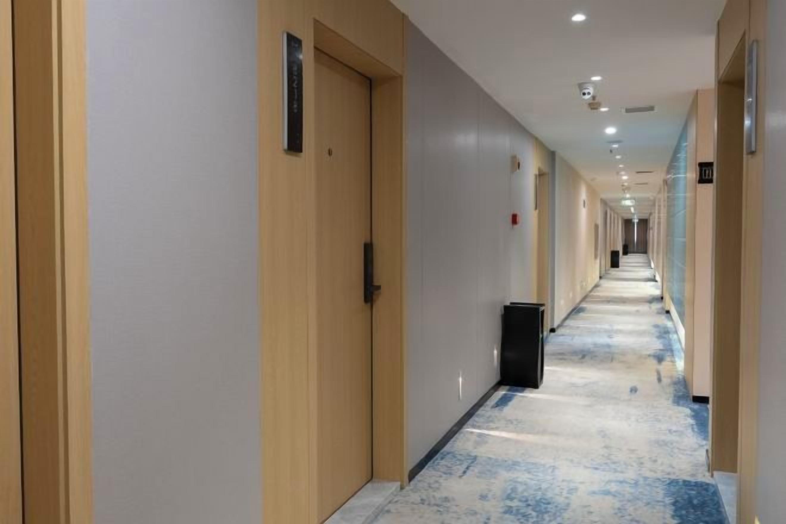 Un corridoio d'albergo con porte su entrambi i lati, un cestino e un pavimento rivestito di moquette.