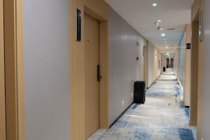 A hotel corridor with doors on both sides, a trash bin, and a carpeted floor. - Longhai Shanghao Huating Holiday Hotel (Zhangzhou)