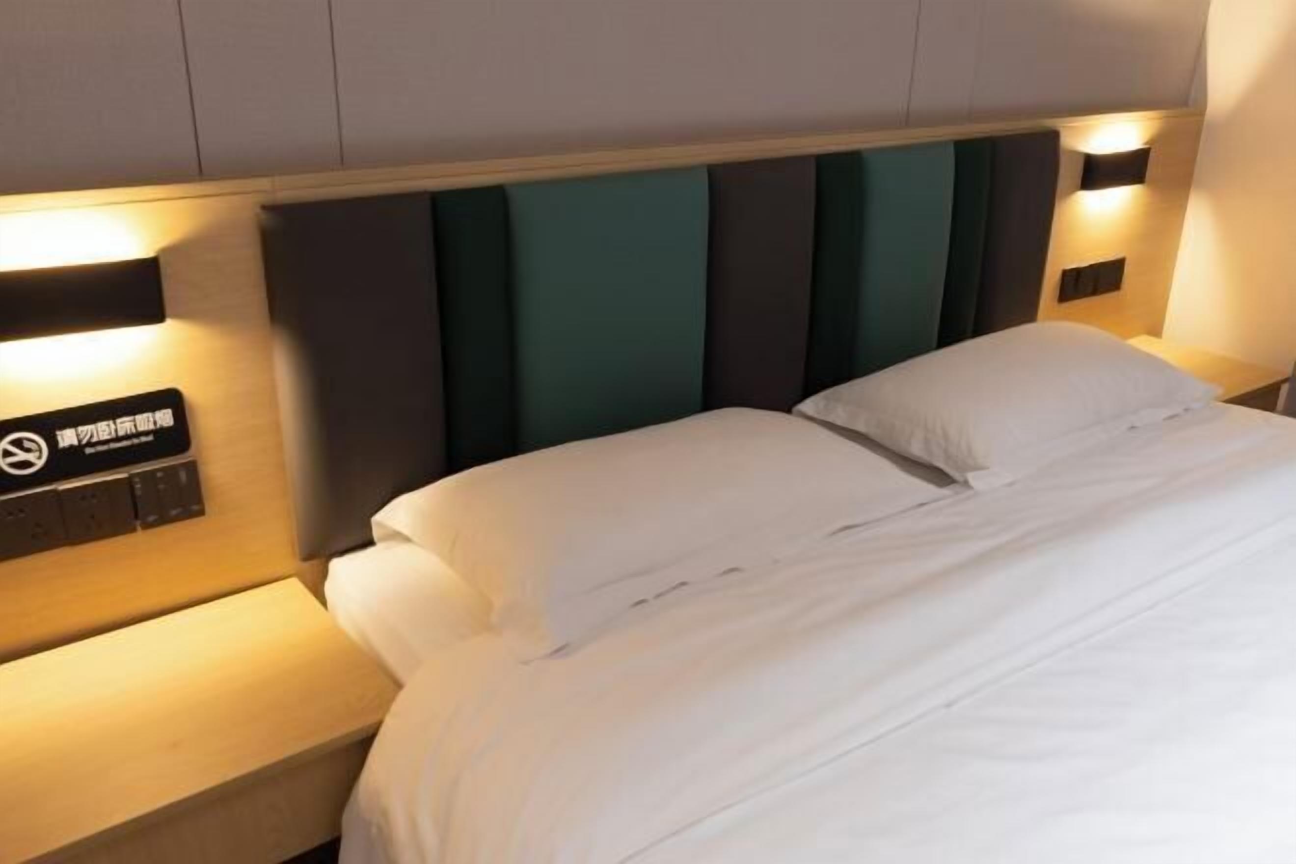 A hotel room with a bed, a nightstand, and a wall-mounted control panel.