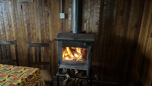 Una habitación con un estufa de leña, una mesa con mantel colorido y paredes de madera.