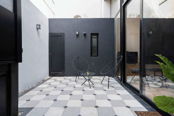 Eine moderne Außenpatio mit Schachbrettboden, zwei Metallstühlen, einer Tür und einer Glaswand.
