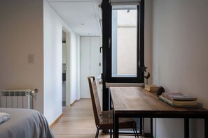 A room with a wooden table, a chair, a radiator, a window with a view, and a door leading to another room.