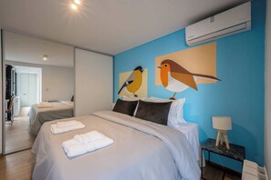 Ein modernes Hotelzimmer mit einem großen Bett, zwei Nachttischen, einer Wand-Klimaanlage und einem Vogelbild.