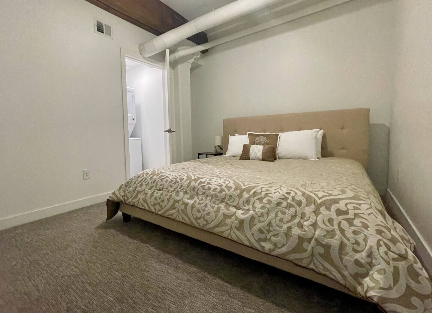 A bedroom with a large bed, a headboard, and a carpeted floor.