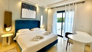 Habitación de hotel con una cama grande, una mesita redonda, un espejo y vistas al exterior.