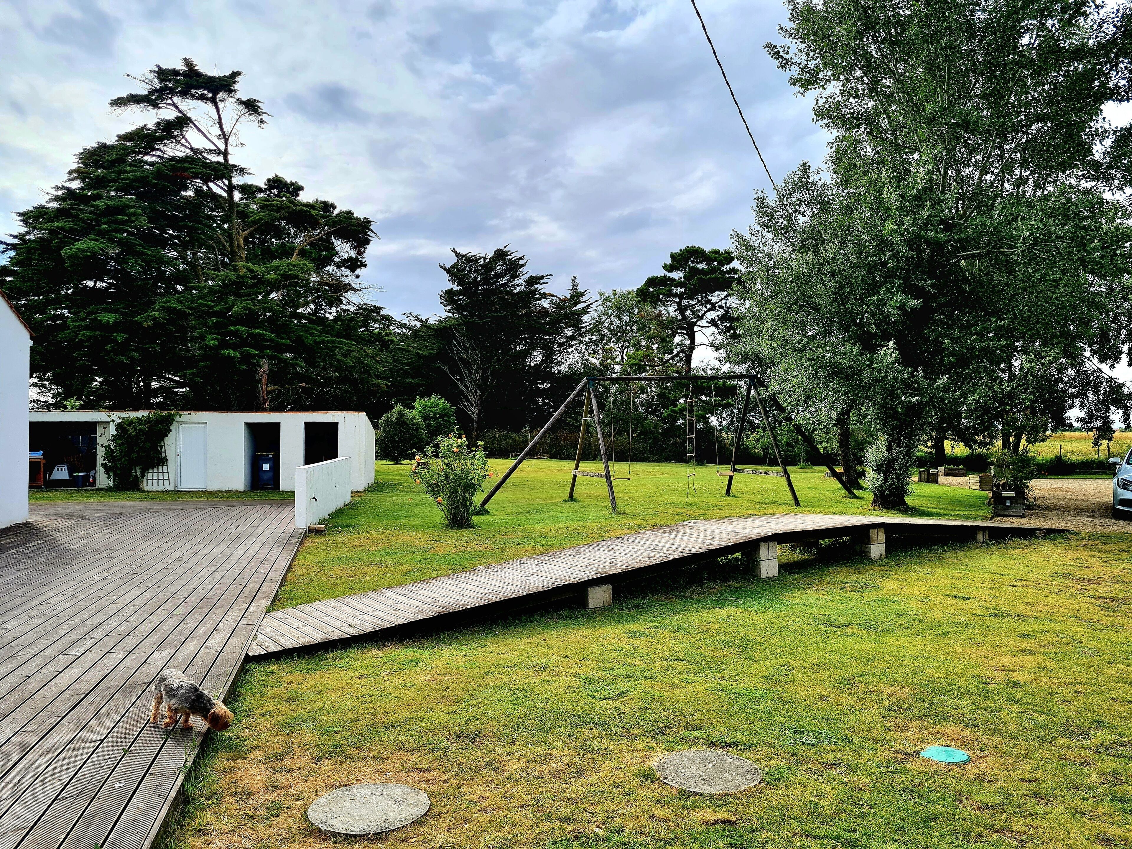 Un jardin avec une terrasse en bois, une balançoire et un petit espace potager.