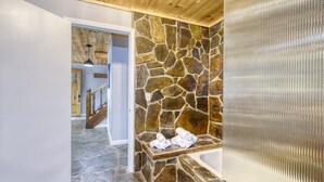 Un baño con pared de piedra, banca de madera y bañera.