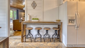 Una cocina con una isla de madera, taburetes de bar, un refrigerador y un suelo de baldosas con diseño.