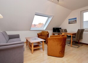Ein modernes Wohnzimmer mit schrägen Wänden, einem Oberlicht, einem Flachbildfernseher, einem Esstisch mit Stühlen und einer Couch.
