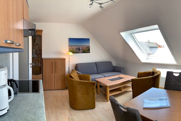 Un espacio habitable compacto con kitchenette, un sofá, una mesa de centro y una mesa de comedor.