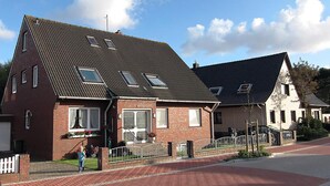 A two-story brick house with a sloped roof, a front porch, and a gated driveway. - Haus Wirdemann Wohnung 2 (Norderney)