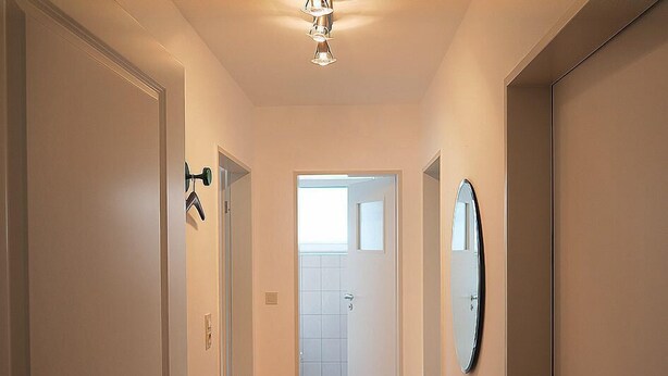 A hallway with a door on the left, a mirror on the right, and a bathroom visible through the door. - Haus Wirdemann Wohnung 2 (Norderney)