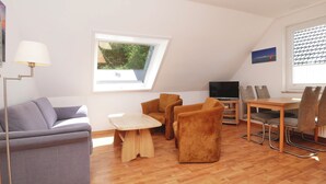A modern living room with a sofa, chairs, a TV, and a dining table. - Haus Wirdemann Wohnung 2 (Norderney)