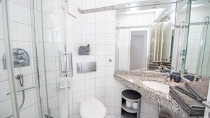 Ein modernes Badezimmer mit einer gläsernen Duschkabine, einer weißen Toilette, einem Waschbecken mit Granitplatte und einem großen Spiegel.