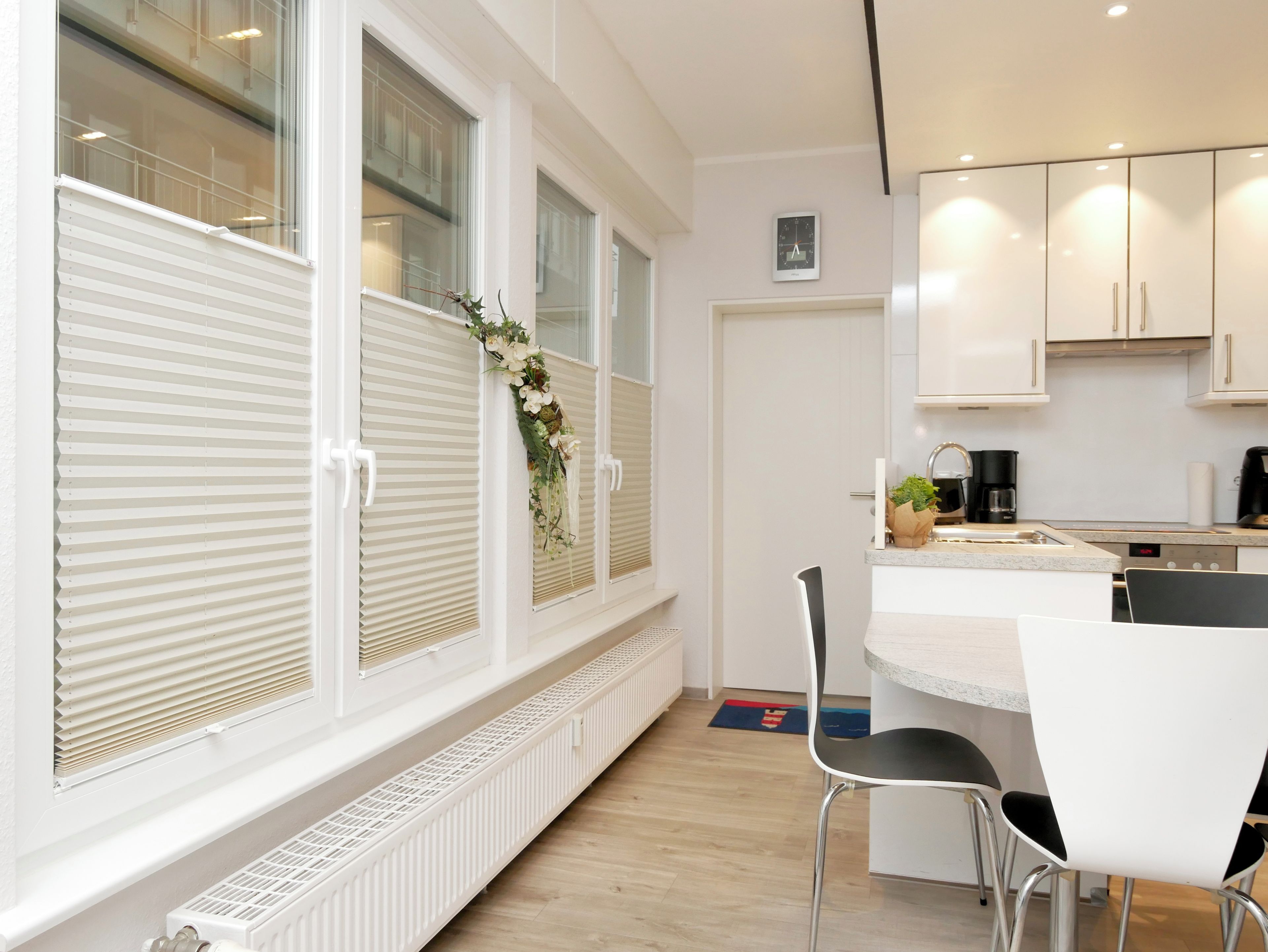A modern kitchen with white cabinetry, a built-in oven, and a window with blinds.