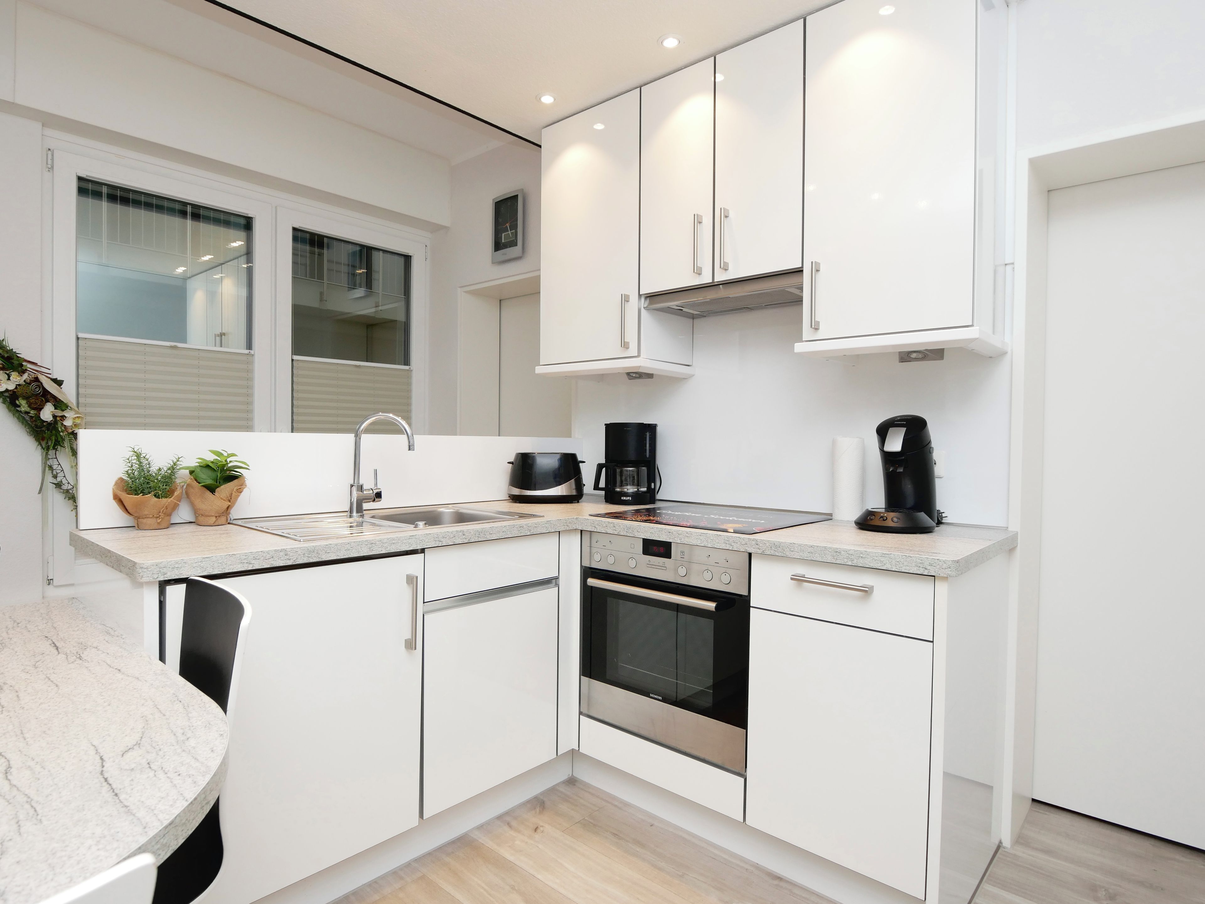 A modern kitchen with white cabinets, a built-in oven, and a coffee maker.