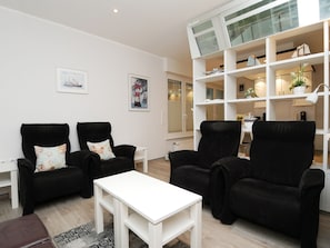 A modern living room with black leather sofas, a white coffee table, and a white shelving unit with decorative items. - Haus Großer Seekaiser (Norderney)