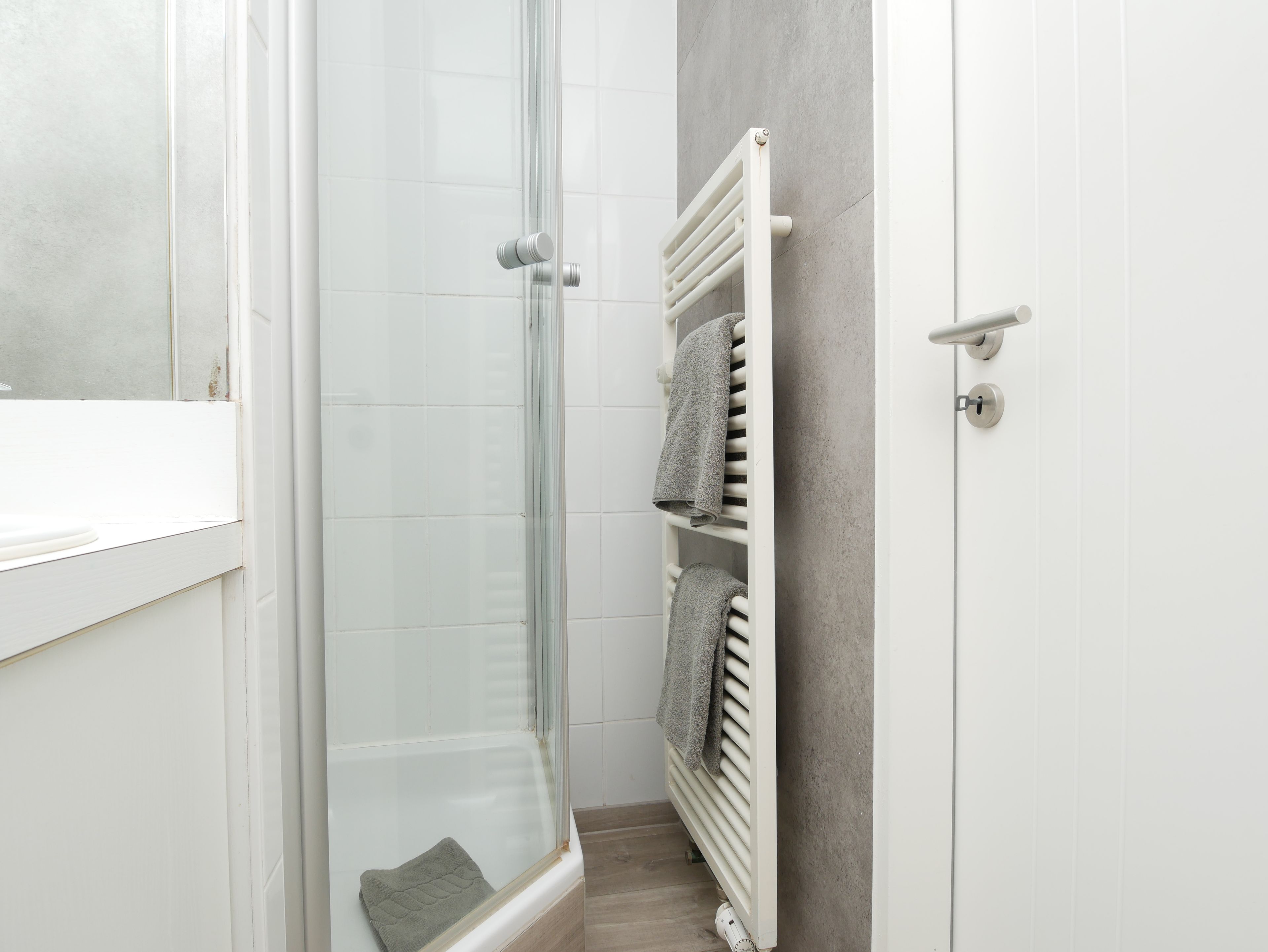 A bathroom with a glass shower enclosure, a white radiator, and a towel rack with towels.