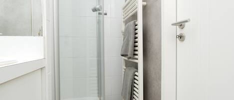 A bathroom with a glass shower enclosure, a white radiator, and a towel rack with towels.