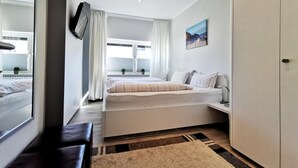 Une chambre à coucher moderne, avec un lit, des tables de chevet, une grande armoire et une vue sur l’extérieur par une fenêtre agrémentée de rideaux.