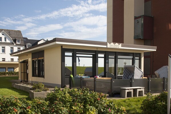 A modern building with large windows, a glass door, and a small patio area with outdoor furniture.
