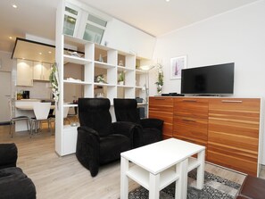 A modern living room with a white sofa, black armchairs, a white coffee table, and a wooden cabinet with a flat-screen TV. - Haus Großer Seekaiser (Norderney)