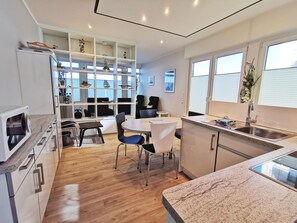 A modern kitchen with a dining area, wooden flooring, and built-in shelving with decorative items.