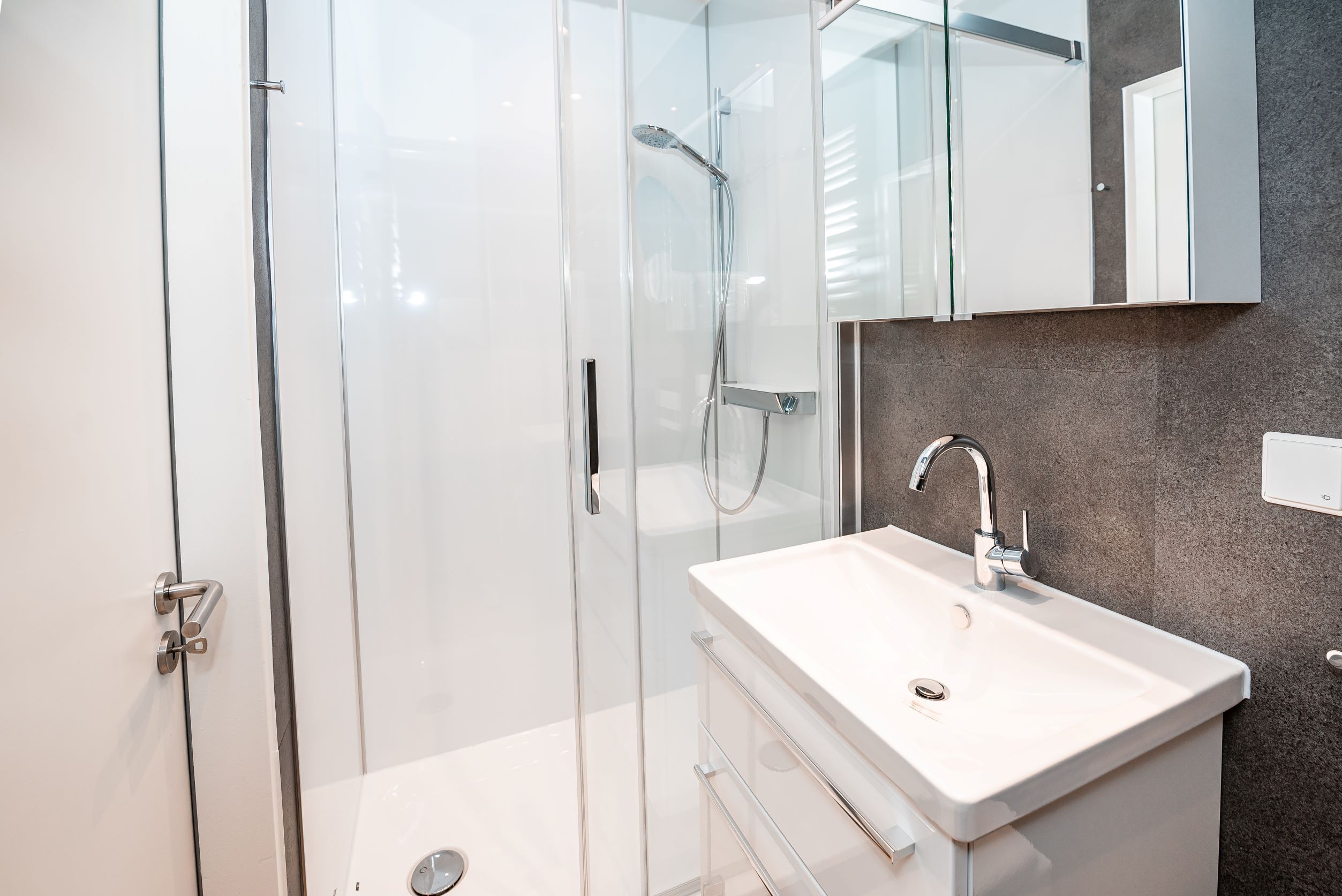 Een moderne badkamer met een douchecabine van glas, een wit wastafelmeubel en een grote spiegel erboven.