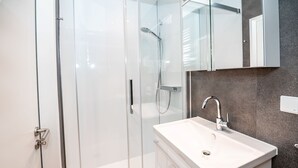 A modern bathroom with a glass shower enclosure, a white sink, and a large mirror above the sink. - House Seekaiser Little Seekaiser (Norderney)