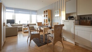 A modern living room with a sofa, dining table, wicker chairs, and a kitchen area with cabinets and a microwave. - House Seekaiser Little Seekaiser (Norderney)