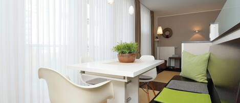 A modern room with a dining table, white chairs, a potted plant, a sofa with green cushions, and a lamp.