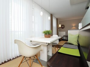 Une pièce moderne comprenant une table à manger, des chaises blanches, une plante en pot, un canapé avec des coussins verts et une lampe.