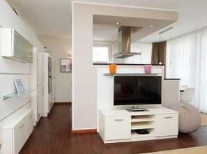 Un salon moderne doté d’un téléviseur à écran plat, d’un coin cuisine intégré et d’un espace détente avec un fauteuil poire.