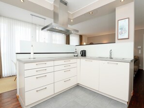 A modern kitchen with white cabinetry, a stainless steel range hood, and a built-in dishwasher. - Düffeldorfer Hof Wohnung A3 / Neyloft (Norderney)