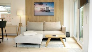 A modern living room with a sofa, a coffee table, a lamp, and a painting on the wall. - Wohnung Nr. 3 / Rübsamen-lüttenberg (Norderney)