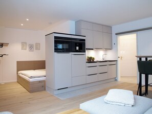 Quarto compacto e moderno, com cama, cozinha compacta e pequena área de refeições.
