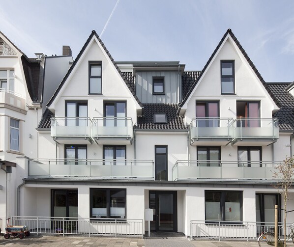 A modern multi-story residential building with balconies, large windows, and a flat roof.